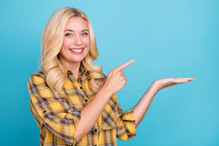 Portrait of lovely cheerful wavy-haired woman holding on palm demonstrating copy space isolated over bright blue color backgroundの写真素材