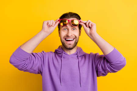 Photo of young excited man amazed shocked happy positive smile ahnds touch glasses isolated over yellow color backgroundの写真素材