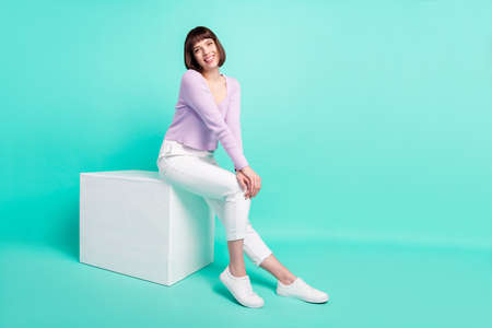 Full length body size photo woman sitting wearing casual outfit smiling cheerful isolated bright turquoise color backgroundの写真素材