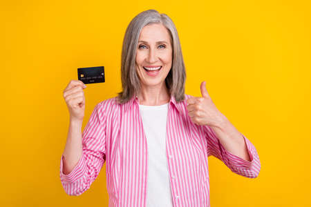 Photo of aged woman happy positive smile show thumb-up like fine ad credit card isolated over yellow...