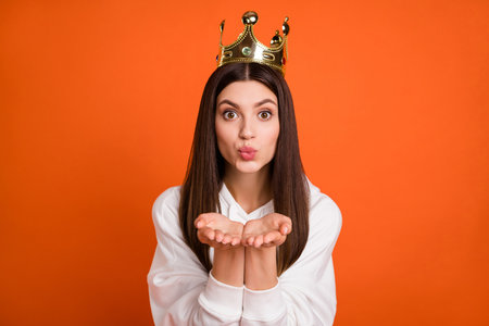Portrait of attractive amorous girl wearing crown sending air kiss isolated over bright orange color backgroundの写真素材