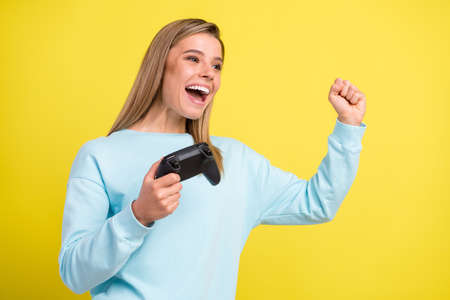 Photo of astonished winner lady hold gamepad raise fist open mouth wear blue pullover isolated on...