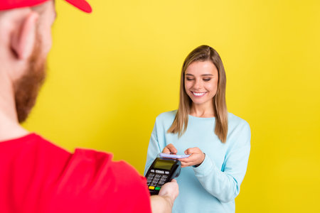 Portrait of attractive cheerful girl getting order paying nfc service isolated over bright yellow color backgroundの写真素材