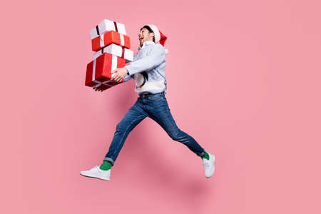 Photo of sweet exited gentleman wear new year sweater smiling jumping high holding gifts stack isolated pink color backgroundの写真素材