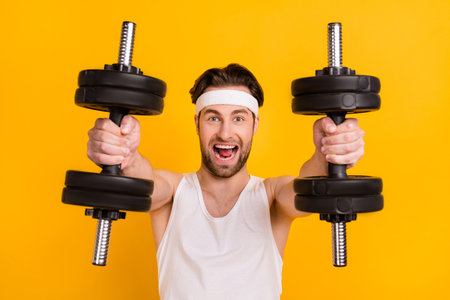 Portrait of attractive endurant strong cheerful guy lifting weight body care isolated over bright yellow color backgroundの写真素材