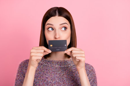 Photo of quiet lady hold debit card close mouth look empty space wear knitted pullover isolated pink...