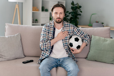 Photo of cute serious guy dressed checkered shirt sitting couch watching football match listening anthem indoors apartment roomの写真素材