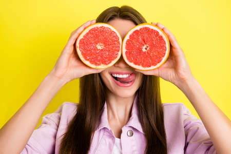 Portrait of attractive cheerful girl closing eyes with grapefruit grimacing fooling isolated over bright yellow color backgroundの写真素材