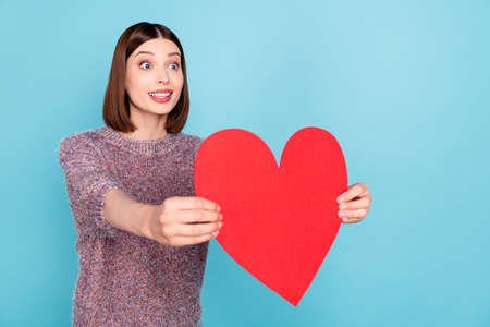 Photo of tempting hopeful lady hold heart card give boyfriend wear knitted sweater isolated blue color backgroundの写真素材
