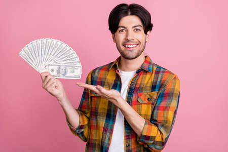 Photo of excited charming young guy dressed checkered clothes holding money fan isolated pink color backgroundの写真素材