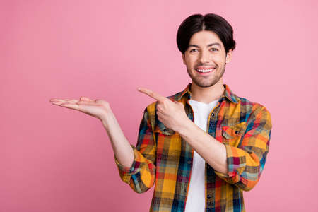 Photo of sweet pretty young gentleman wear plaid outfit holding arm pointing finger empty space smiling isolated pink color backgroundの写真素材