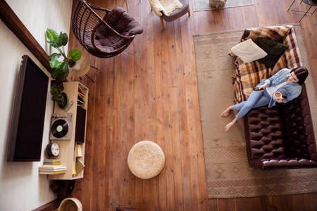 Top above high angle view of attractive girl sitting on sofa drinking cacao watching tv show series dream life at home open space indoorsの写真素材