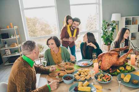 Portrait of attractive careful cheerful big full family eating festal turkey dish meal talking speaking having fun at home indoorsの写真素材