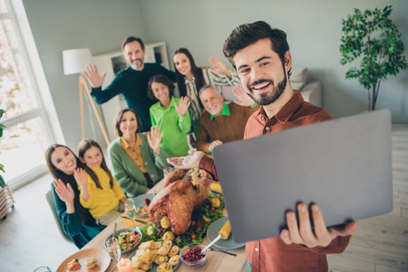 Photo of adorable funny family celebrating thanks giving day sitting table talking modern device smiling indoors room homeの写真素材
