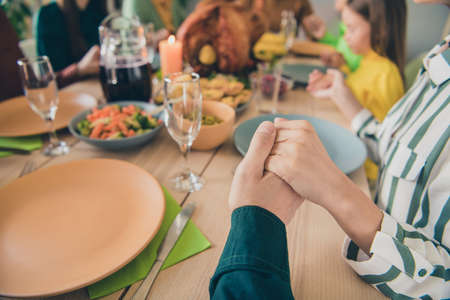 Cropped view portrait of adorable dreamy family holding hands praying appreciating eating lunch at home indoorsの写真素材