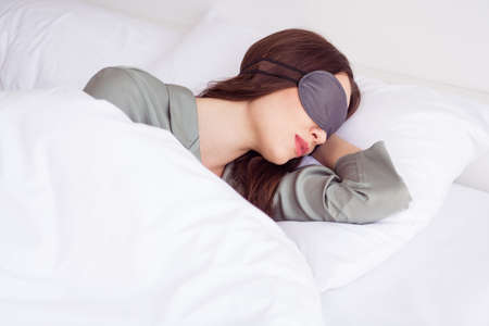 Photo of charming tired young lady grey sleepwear lying bed mask cover eyes indoors room homeの写真素材