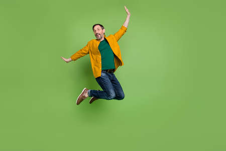 Full length photo of happy cheerful mature man jump up enjoy weekend smile isolated on green color backgroundの写真素材