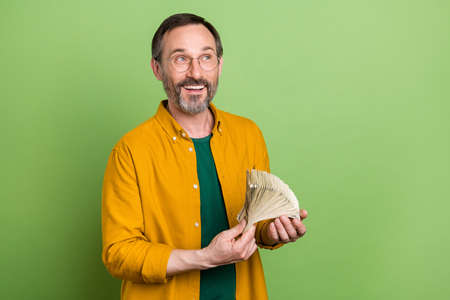 Photo of mature business man happy positive smile hold cash dollars money rich look empty space isolated over green color backgroundの写真素材