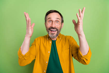 Photo of excited sweet age gentleman wear orange shirt spectacles rising arms isolated green color backgroundの写真素材