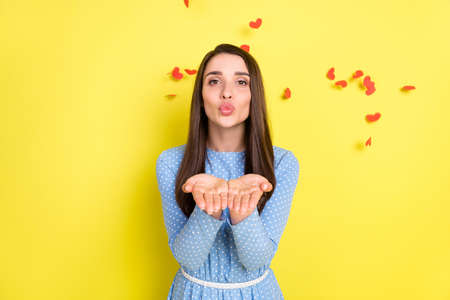 Photo of romantic affectionate girl hold hands send air kiss wear dotted blue dress isolated yellow...