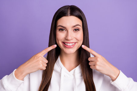 Photo of young positive happy woman point fingers face teeth whitening smile isolated on violet...