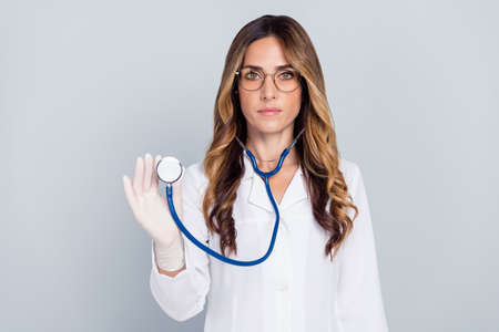Portrait of attractive experienced wavy-haired woman doc using stethoscope isolated over grey pastel color backgroundの写真素材