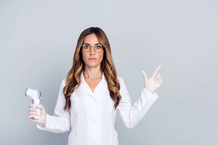 Photo of mature serious woman point finger empty space thermometer wear uniform gloves isolated on grey color backgroundの写真素材
