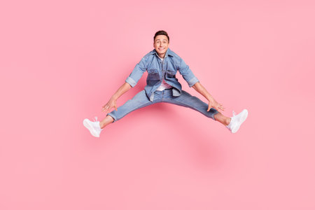 Full size photo of young funky funny careless smiling guy jumping rejoice energetic isolated on pink color backgroundの写真素材