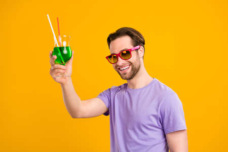 Photo of cute pretty gentleman wear violet t-shirt dark eyewear smiling inviting drinking cocktail isolated yellow color backgroundの写真素材