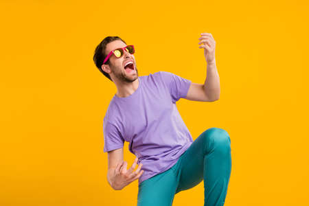Photo of careless rocker guy play imaginary guitar scream wear sunglass purple t-shirt isolated yellow color backgroundの写真素材