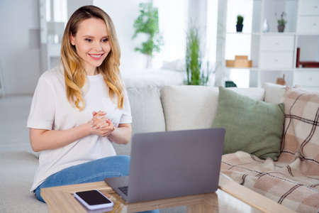 Portrait of attractive cheerful girl using laptop watching video cinema film at light white home...