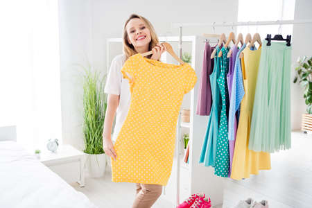 Portrait of attractive carefree cheerful blond girl choosing dress having fun rest free time at light white home indoorsの写真素材