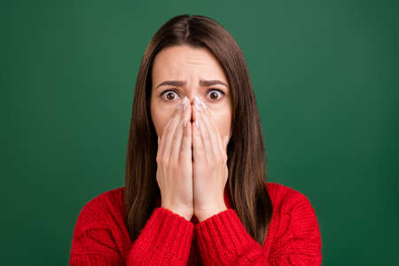 Photo portrait girl in red pullover covered face with hand amazed keeping secret isolated green...