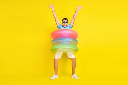 Photo of excited cute young man wear blue t-shirt dark glasses standing inside water circles smiling isolated yellow color backgroundの写真素材