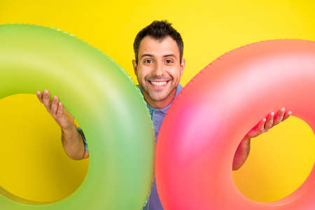 Photo of funny brunet man hold circles wear blue t-shirt isolated on yellow color backgroundの写真素材