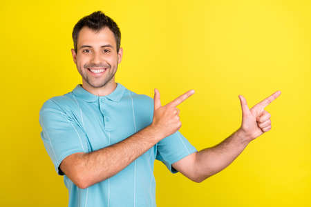 Photo of funny charming young man wear blue t-shirt pointing fingers empty space smiling isolated yellow color backgroundの写真素材