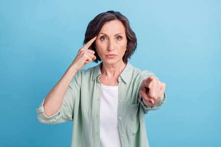 Photo portrait senior woman in shirt selecting you keeping finger near forehead isolated pastel blue color backgroundの写真素材