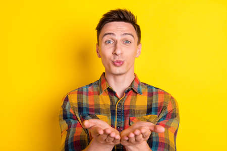 Portrait of attractive cheery funny guy sending you air kiss isolated over vibrant yellow color...