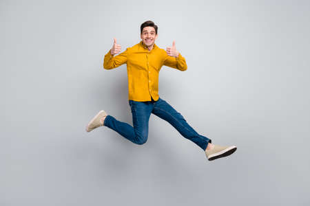 Full length body size view of attractive cheerful man jumping showing thumbup isolated over grey...