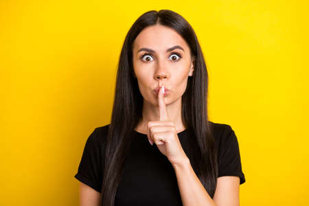 Photo portrait of woman keeping finger near lips secret isolated vibrant yellow color backgroundの写真素材