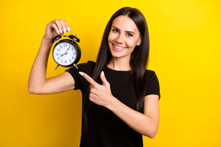 Portrait of pretty positive girl indicate finger hand hold classic clock beaming smile isolated on yellow color backgroundの写真素材