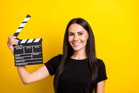 Photo of positive young girl arm hold clapboard have good mood look camera isolated on yellow color backgroundの写真素材