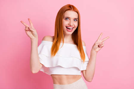 Portrait of attractive cheerful girlish red-haired girl showing double v-sign having fun isolated...