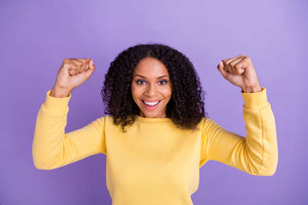 Photo of pretty lucky dark skin woman dressed yellow sweater smiling rising fists isolated violet...