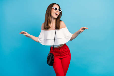 Photo of funky brunette young lady look empty space wear spectacles white top jeans bag isolated on blue color backgroundの写真素材