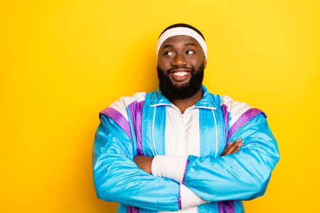 Photo of cute dreamy dark skin guy dressed sport suit headband smiling arms crosse looking empty space isolated yellow color backgroundの写真素材