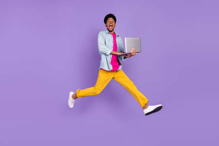 Photo of programmer guy jump hold netbook hurry late wear blue shirt pants shoes isolated purple color backgroundの写真素材