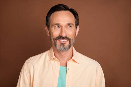 Photo of mature brunet man optimistic look empty space wear peach shirt isolated on brown color backgroundの写真素材