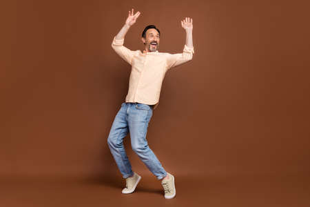 Photo of carefree dreamy guy dance raise hands stand tiptoe wear beige shirt jeans shoes isolated...