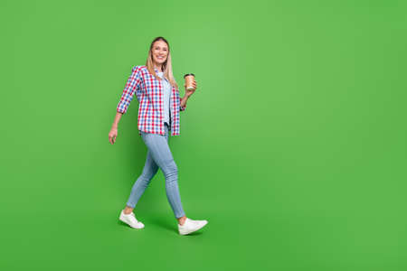 Full body profile side photo of young woman happy positive smile go walk drink coffee isolated over green color backgroundの写真素材
